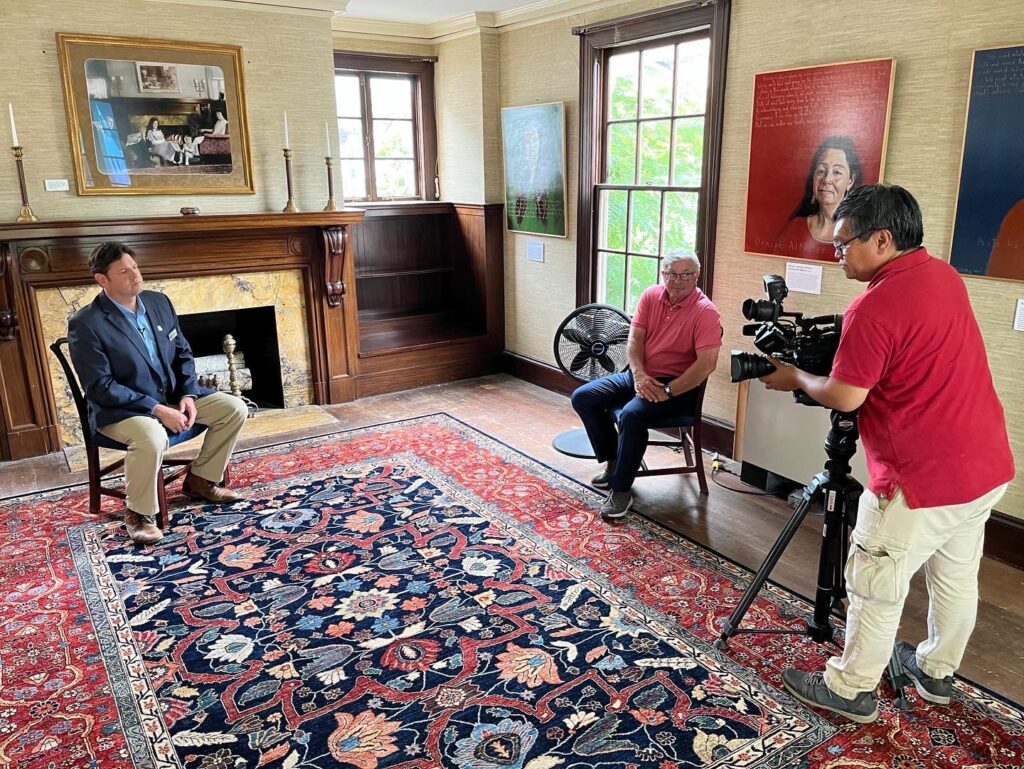 Museum CEO Christian Cotz sits in museum's library with Total Maine host Steve Minich. A man points a camera at the two.